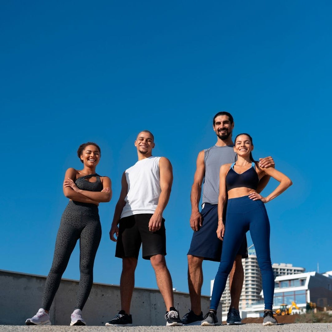 Four people in athletic wear standing together outdoors against a clear blue sky, with a low concrete wall and distant buildings behind them.